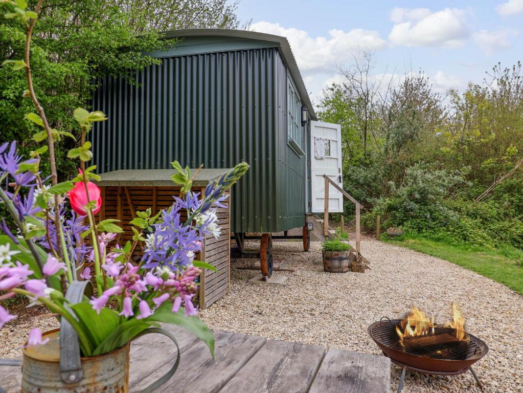 a garden with a green shed and some flowers at Oak Shepherd Hut in Bridport
