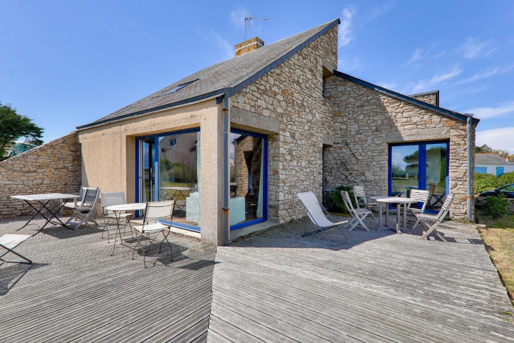 a wooden deck with chairs and tables and a building at Vue mer et acces plage direct pour 11 personnes in Saint-Gildas-de-Rhuys