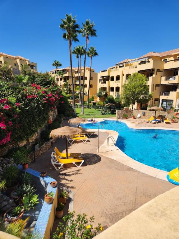 a resort pool with chairs and umbrellas and palm trees at Green Hill Apartment in La Cala de Mijas