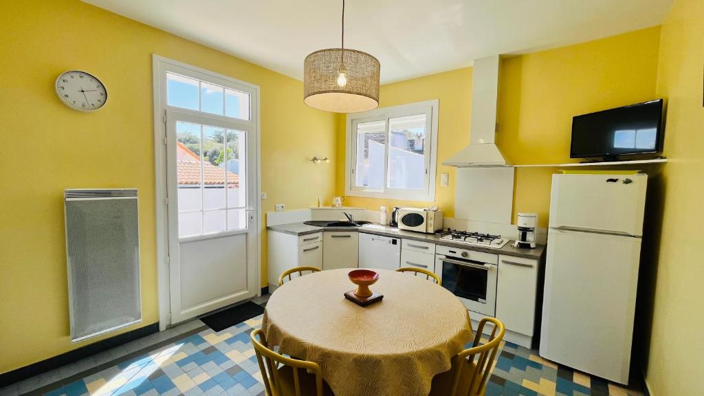 - une cuisine avec des murs jaunes, une table et un réfrigérateur dans l'établissement Les Alouettes centre ville et mer, à Saint-Jean-de-Monts