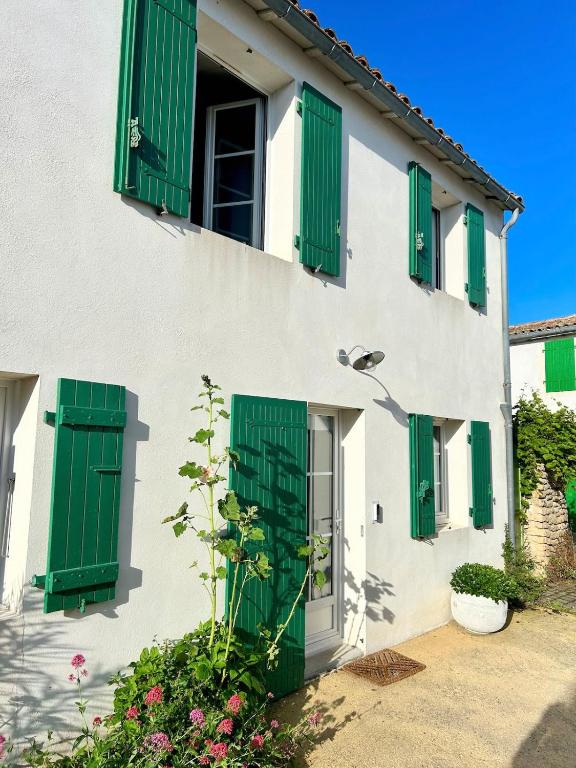 un bâtiment blanc avec des volets verts et des fleurs dans l'établissement Le Nid des Salants, à Loix