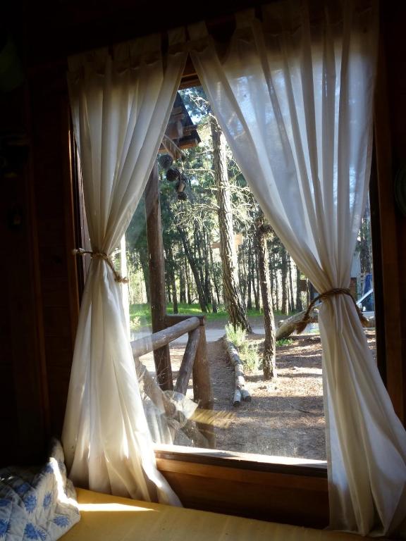 a window with white curtains and a view of a yard at Cabaña Kultrum Mar Azul in Mar Azul