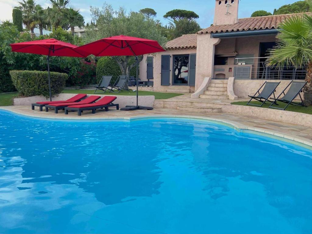 une piscine avec deux parasols rouges et une maison dans l'établissement Vivre Sainte-Maxime à pieds, à Sainte-Maxime