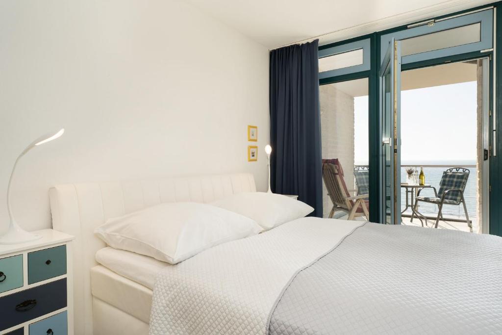 a white bedroom with a bed and a balcony at Am Südstrand 9 Strandburg II in Fehmarn