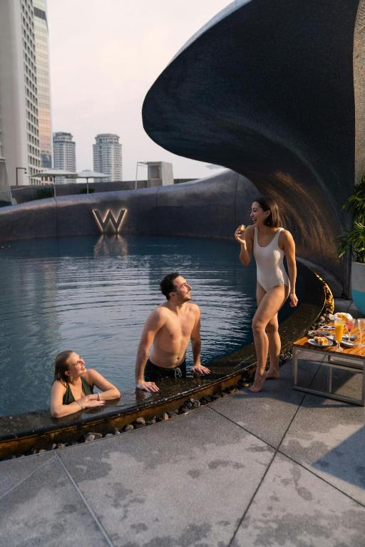 Guests gather in a rooftop-style pool beneath a sculptural curved canopy.
