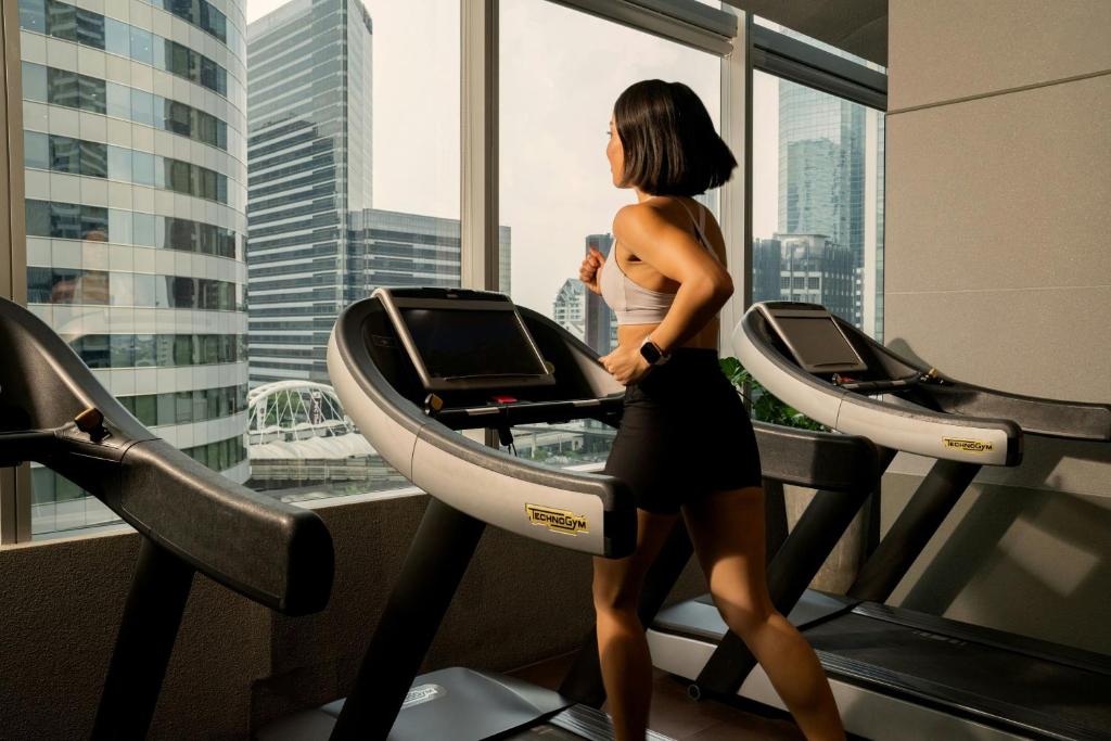 A high-floor gym lined with treadmills and large windows overlooking Bangkok’s surrounding towers.