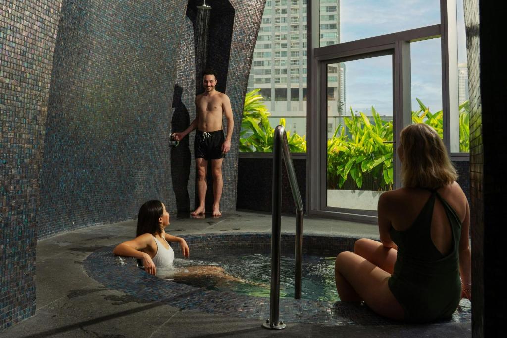 A tiled indoor-outdoor jacuzzi with a window onto greenery and neighboring high-rise buildings.
