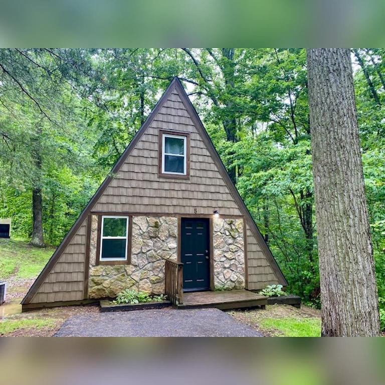 a small house with a triangular roof in the woods at A-Frame #05 - by The Chalets in Logan