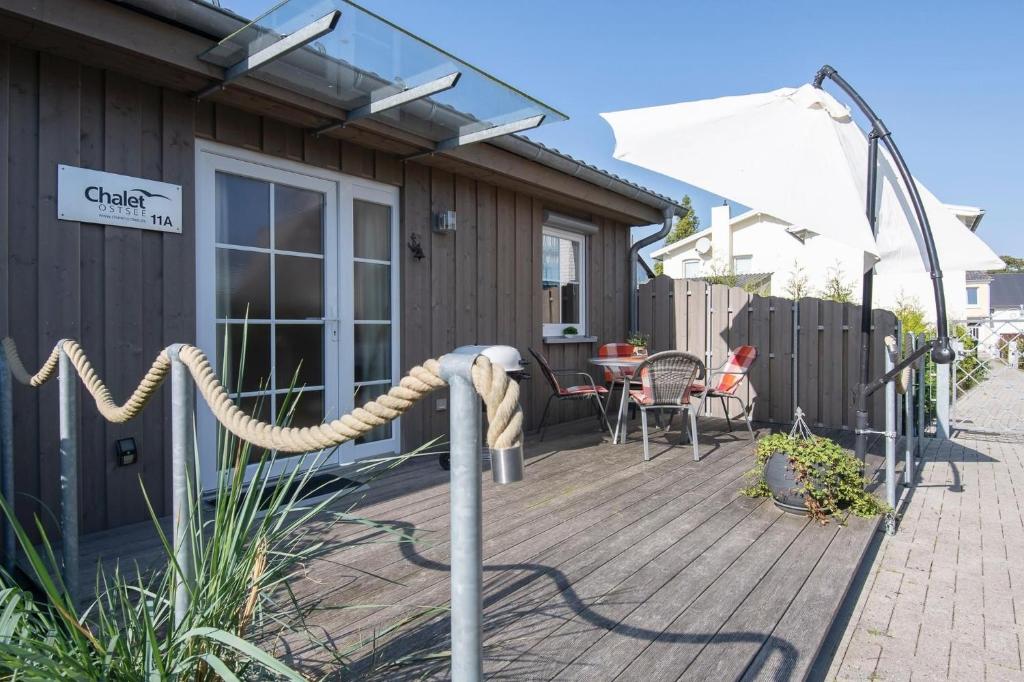 una terraza de madera con mesa y sombrilla blanca en Chalet Ostsee A, en Dahme