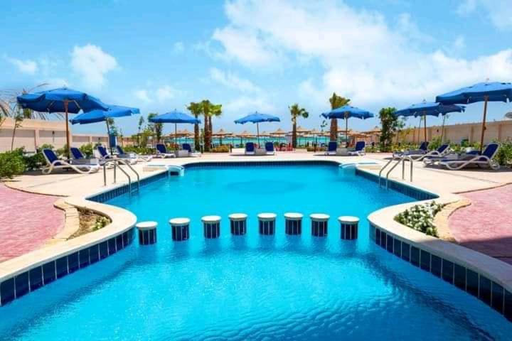 a large swimming pool with blue umbrellas and chairs at Casablanca Beach for families only in Hurghada