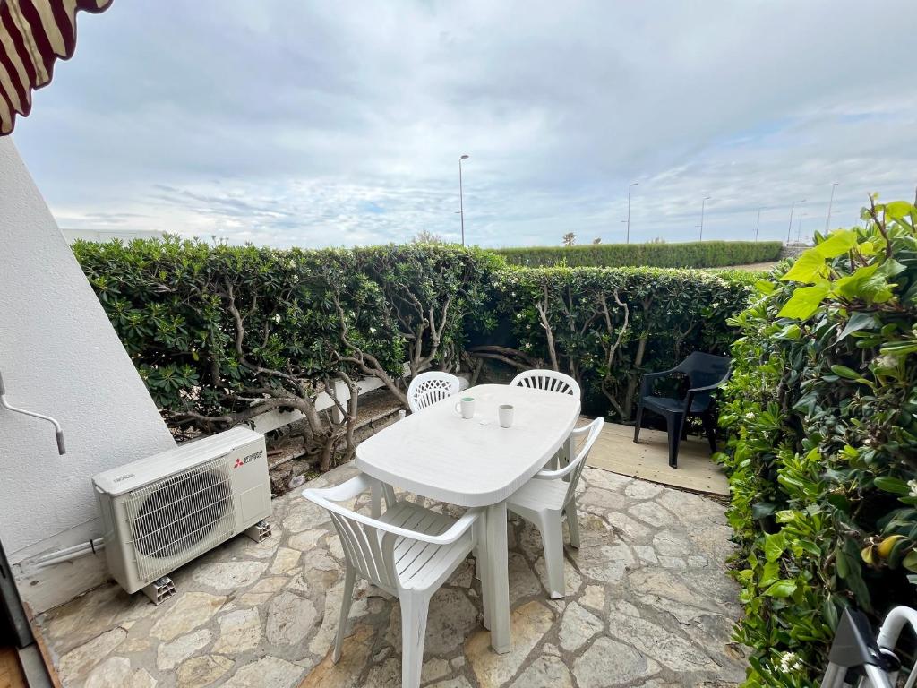 un patio avec une table et des chaises blanches et des buissons dans l'établissement Studio climatisé pour 2 avec terrasse et parking près des plages - FR-1-338-613, à Sète