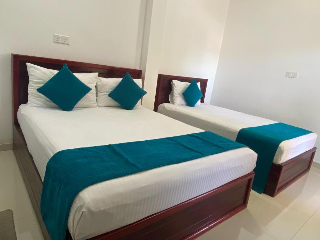 two beds in a hotel room with blue pillows at Travel Lodge City Hotel in Trincomalee