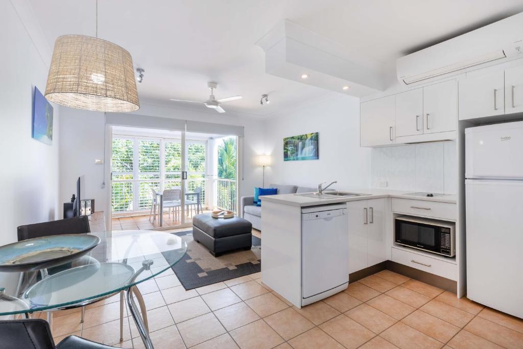 eine Küche und ein Esszimmer mit weißen Schränken und einem Tisch in der Unterkunft Port Douglas Apartments - Adults Only Oasis in Port Douglas