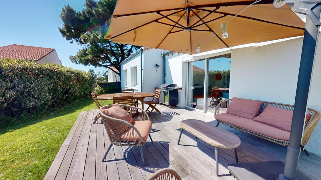 une terrasse en bois avec un canapé et un parasol dans l'établissement La Perle de L Auzance, à Brem-sur-Mer
