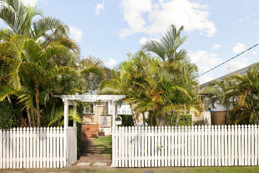 a white fence in front of a house with palm trees at Smart Suites Self Check-In Cottage - Carina in Brisbane