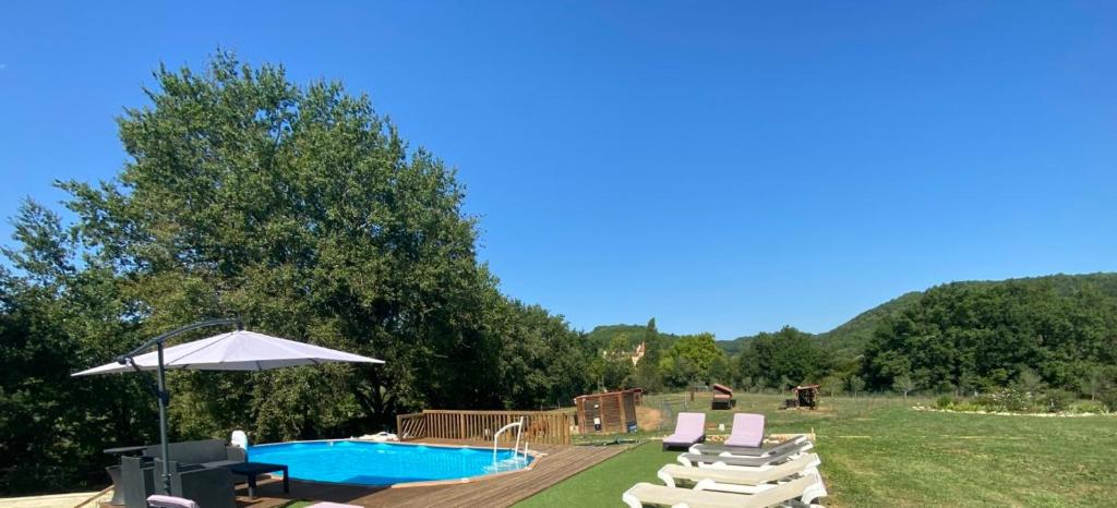 a backyard with a pool and chairs and an umbrella at La Bergerie Luxury cottage and pool on eco-friendly micro-farm in Duravel