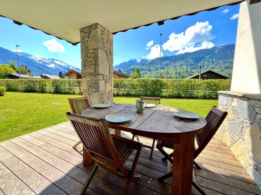 une table en bois avec quatre chaises sur une terrasse en bois dans l'établissement Appartement de charme avec terrasse, piscine et parking, proche centre et arrêt ski-bus - FR-1-624-105, à Samoëns