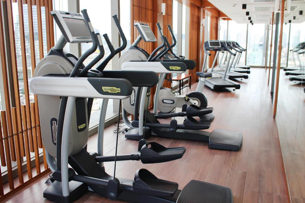 A bright cardio area with ellipticals and treadmills beside tall windows.