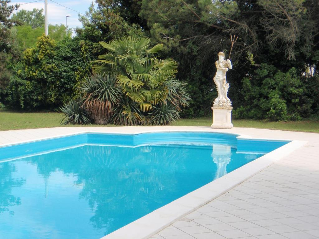 une statue assise à côté d'une piscine bleue dans l'établissement Villa Carrer, à Porto Viro