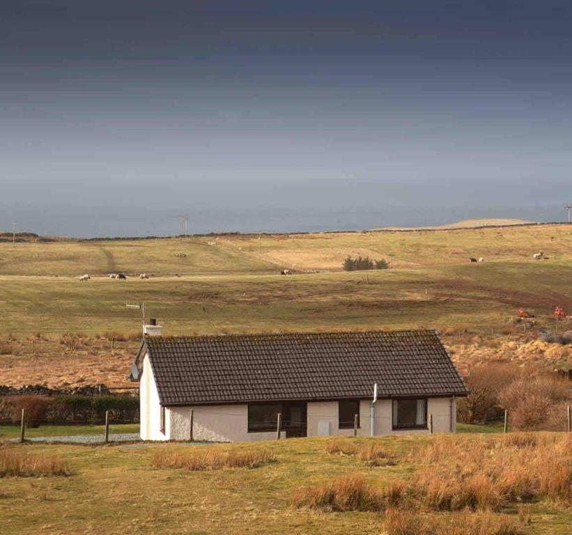 a small white house in the middle of a field at Ardmore Holiday Cottage in Trumpan