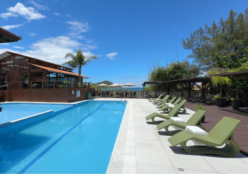 a swimming pool with chaise lounge chairs and the ocean at Village Praia do Rosa in Praia do Rosa