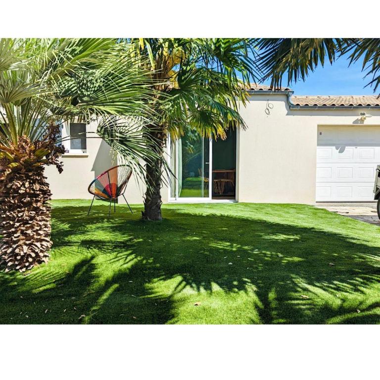 une maison avec un palmier et une chaise dans la cour dans l'établissement Charme et Confort à Lagord, à Lagord