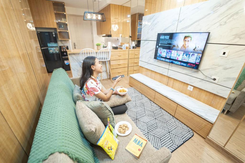 ein junges Mädchen sitzt auf einer Couch und sieht fern in der Unterkunft Kamilla's Stay - 2 Bed Rooms Apartment in Kejayan