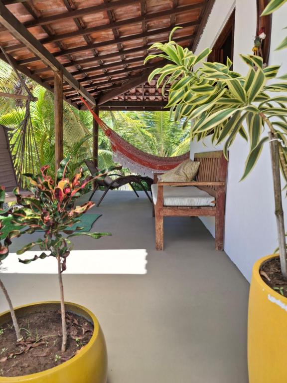 a porch with two potted plants and a hammock at Recanto Verde - Praia de Santo Antônio in Diogo