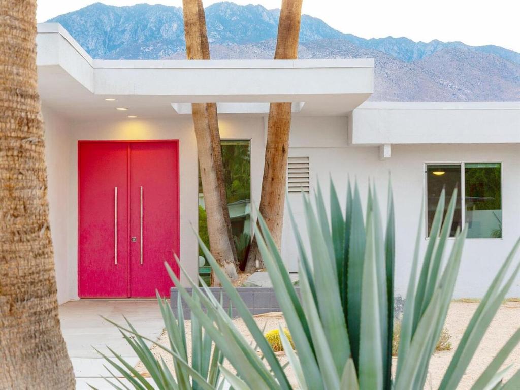 a red door on a house with palm trees at As seen on HGTV Desert Flippers The Pink Door in Palm Springs