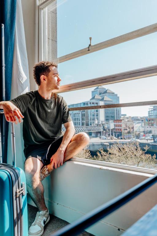 a man sitting on a ledge looking out a window at Eden Quay Guesthouse Private Rooms in Dublin