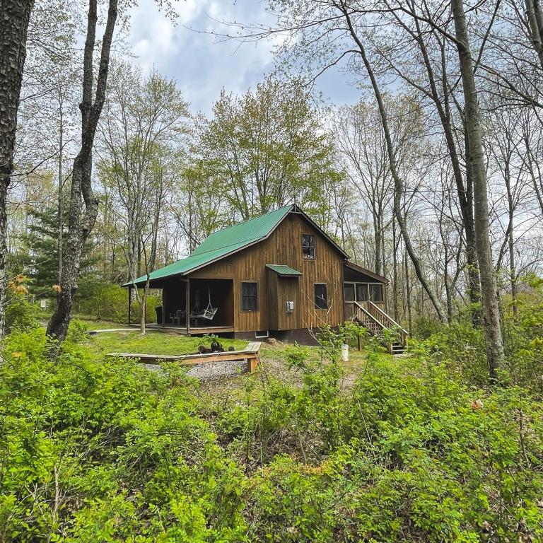 a wooden cabin with a green roof in the woods at Hawks Peak - by The Chalets in Logan