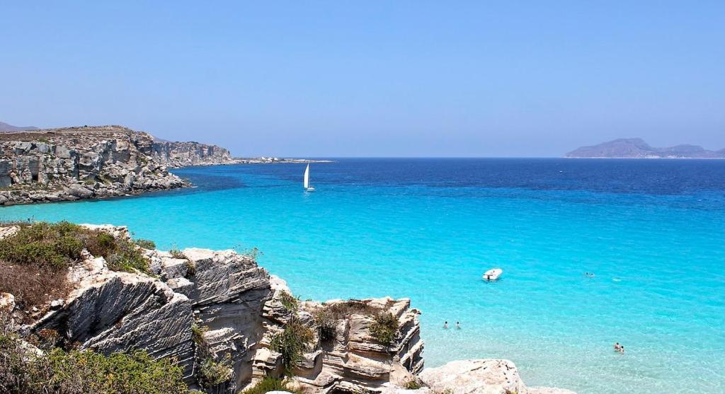 a beach with people swimming in the blue water at Favignana in centro con terrazza in Favignana