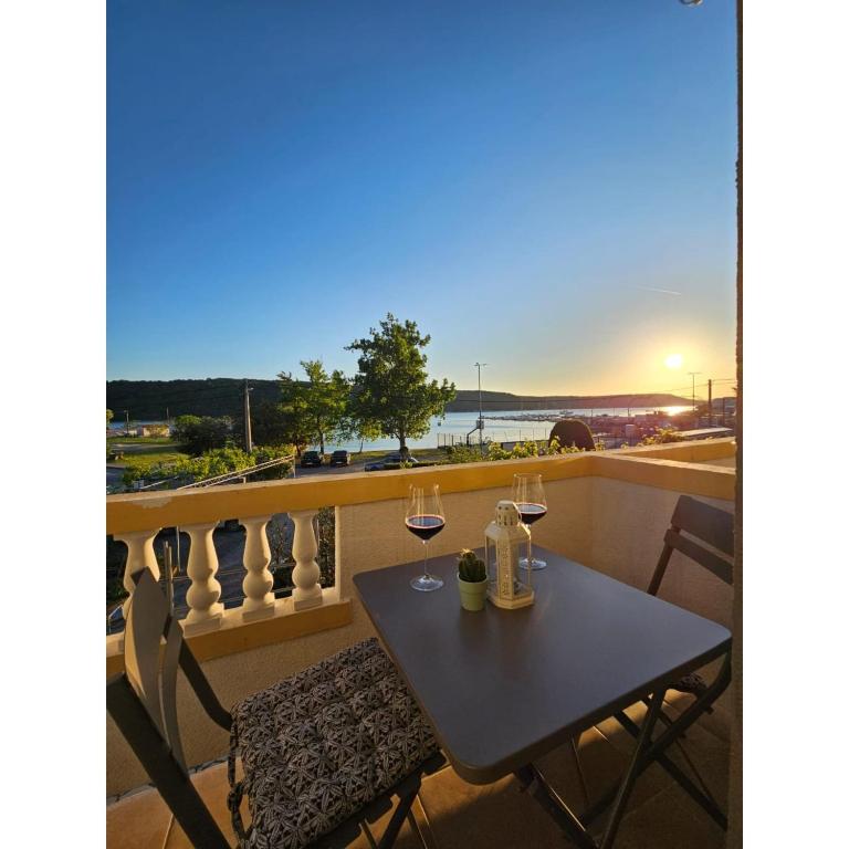 a table and chairs on a balcony with wine glasses at Apartmani Huno in Kampor