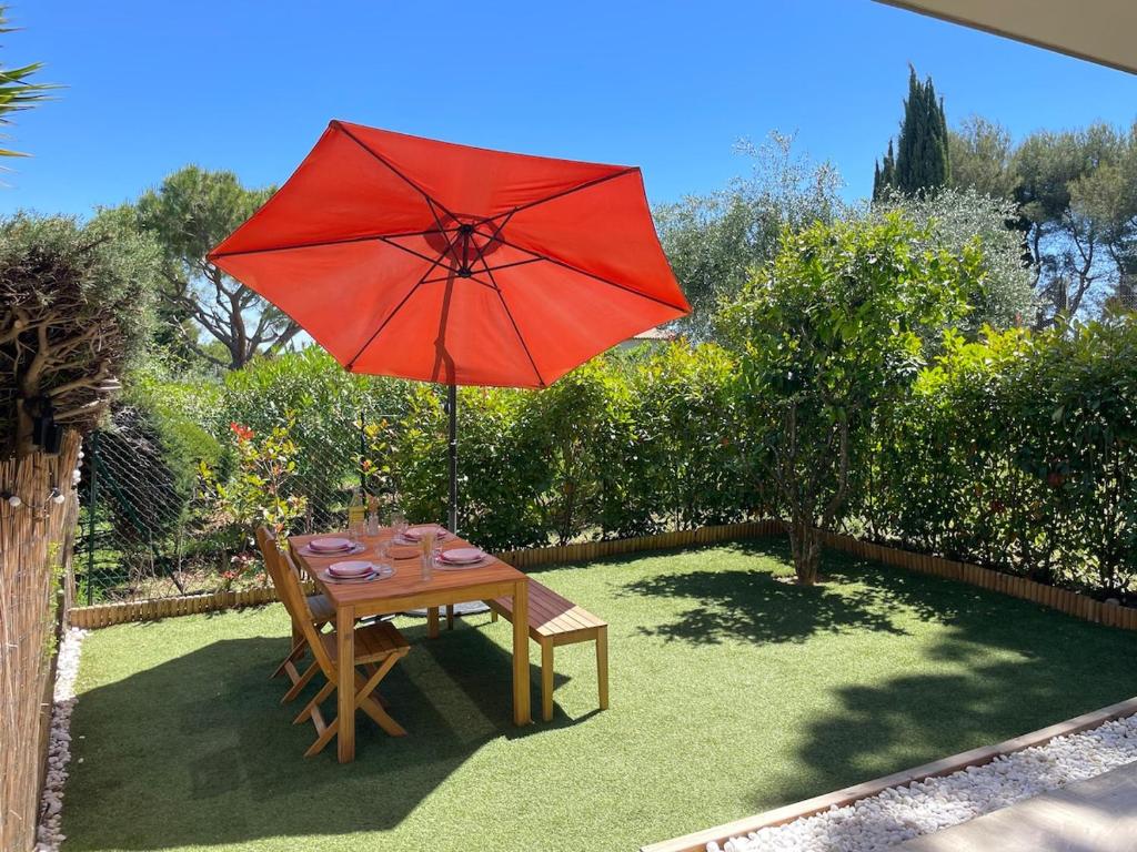 - une table avec un parasol rouge dans le jardin dans l'établissement Appartement - Chez Laura, à Villeneuve-Loubet