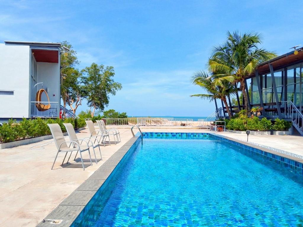 a pool with chairs and the ocean in the background at Sunset Serenity Jomtien Resort in Na Jomtien