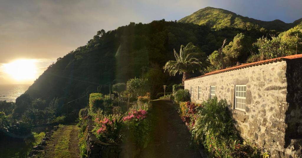 a stone building on a hill with the sun setting at Vistalinda Farmhouse in Fajã dos Vimes