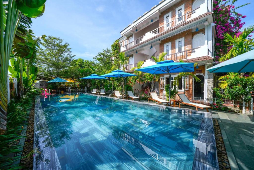 会安Ancient Garden Boutique Hoi An的一座带有蓝色遮阳伞的建筑前有一个大型游泳池