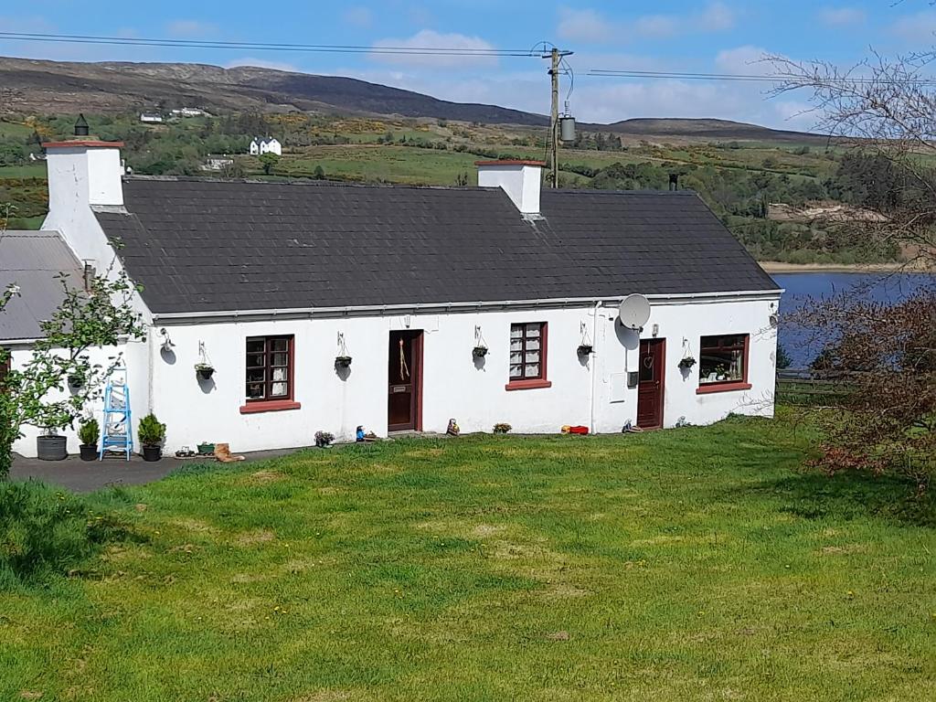 a white house with a black roof on a lawn at Granny's cottage, a lovely lakeside cottage in Donegal