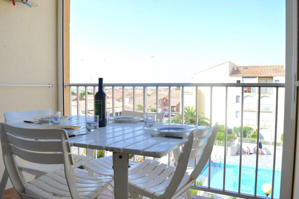 - une table avec des chaises blanches et une bouteille de vin sur le balcon dans l'établissement NP170-C068 Appartement 2 pièces mezzanine, Narbonne Plage, à Narbonne-Plage