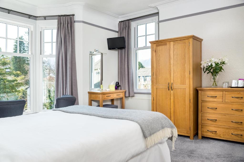 a bedroom with a bed and a dresser and windows at Skiddaw Croft Bed & Breakfast in Keswick