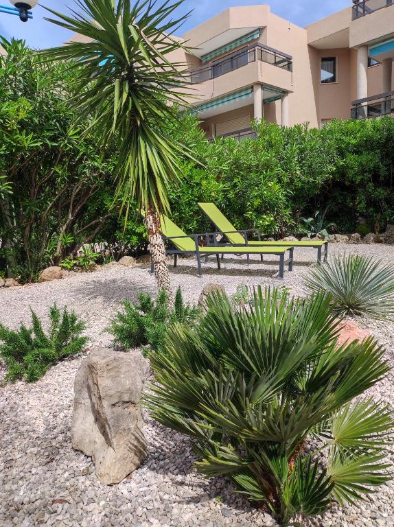 un jardin avec des chaises et des palmiers en face d'un bâtiment dans l'établissement Le Palmier, jardin privatif, plage 200m, classé 3 étoiles, wifi, garage,rénové en 2024, à Cavalaire-sur-Mer