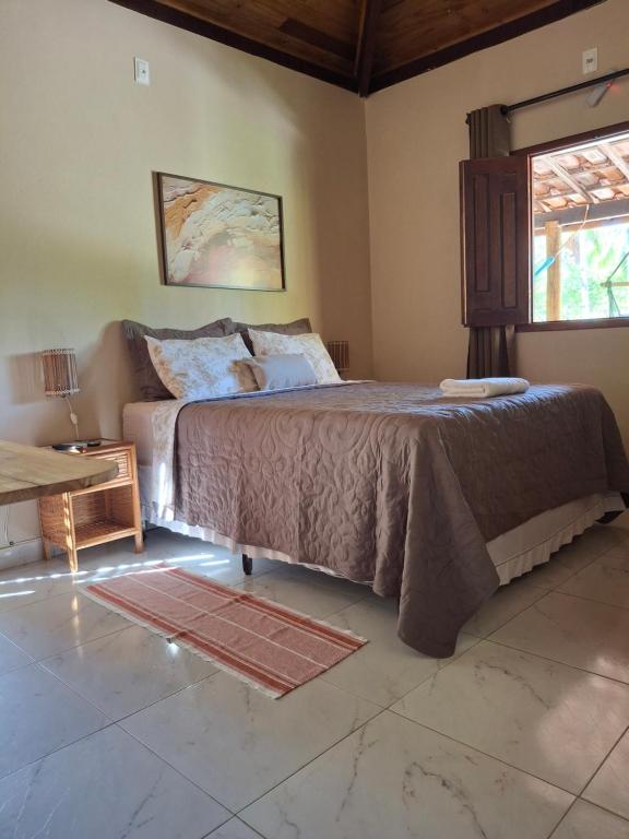 a bedroom with a bed and a table and a window at Recanto Verde - Praia de Santo Antônio in Diogo