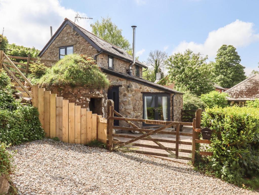 an old stone cottage with a wooden gate and fence at Ash Cottage in Newton Abbot