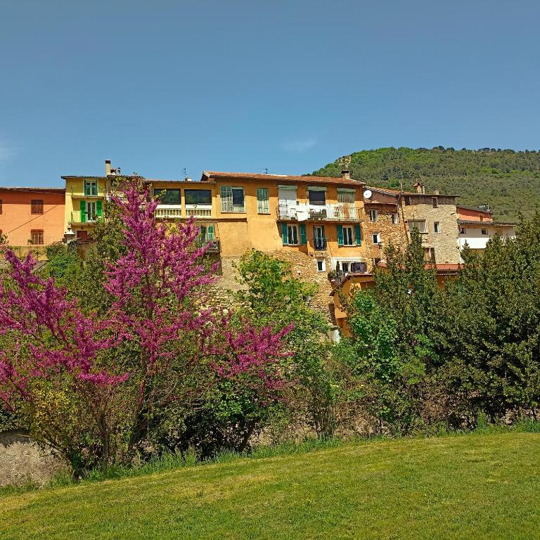 un bâtiment en arrière-plan avec des fleurs violettes et des arbres dans l'établissement apartement des Romains, à Sospel