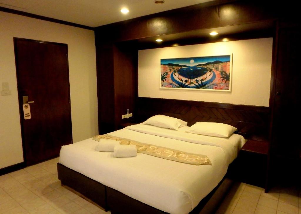a bedroom with a large white bed with a painting on the wall at Karon Cafe Inn in Karon Beach