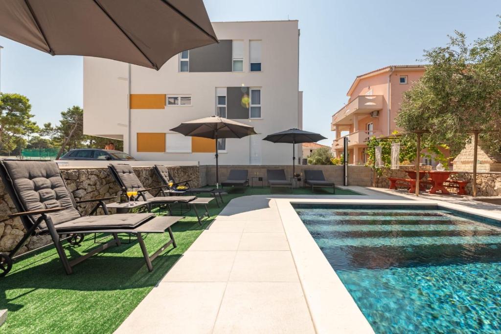 Una piscina con sillas y sombrillas al lado de un edificio. en Villa Pagus with pool and private parking, en Novalja