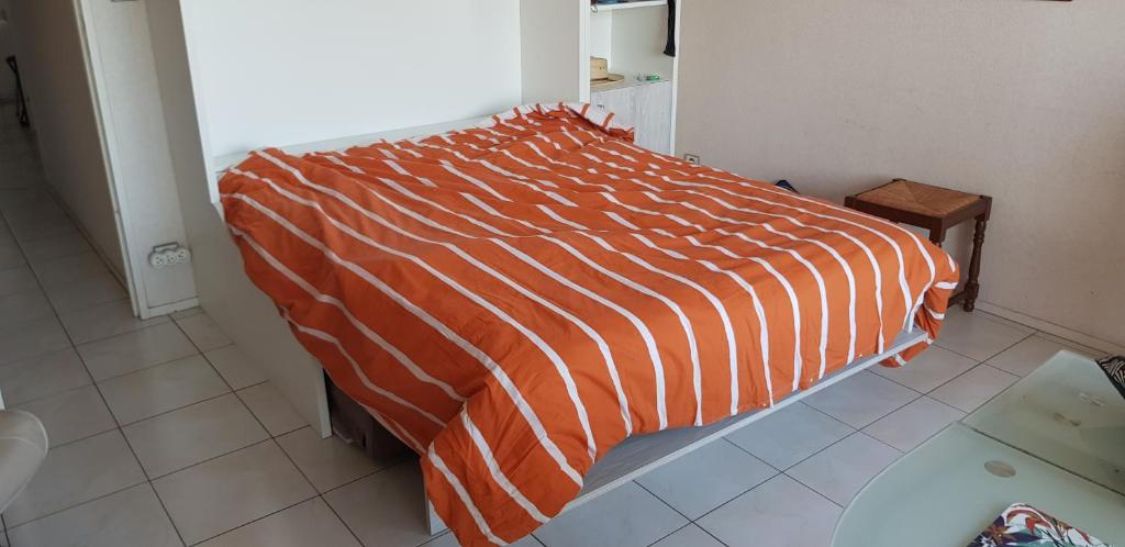 un lit avec une couette rayée orange et blanche dans une chambre dans l'établissement Residence grand voile avec vue bassin, à Arcachon