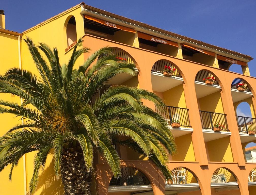 un edificio amarillo con una palmera delante en Hotel Alhambra, en Cap d'Agde