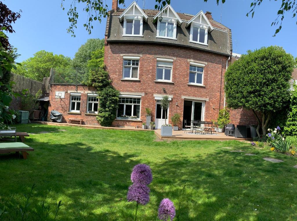 une grande maison en briques avec une cour verte avec des fleurs violettes dans l'établissement Chambre au petit Chateau, à Tourcoing