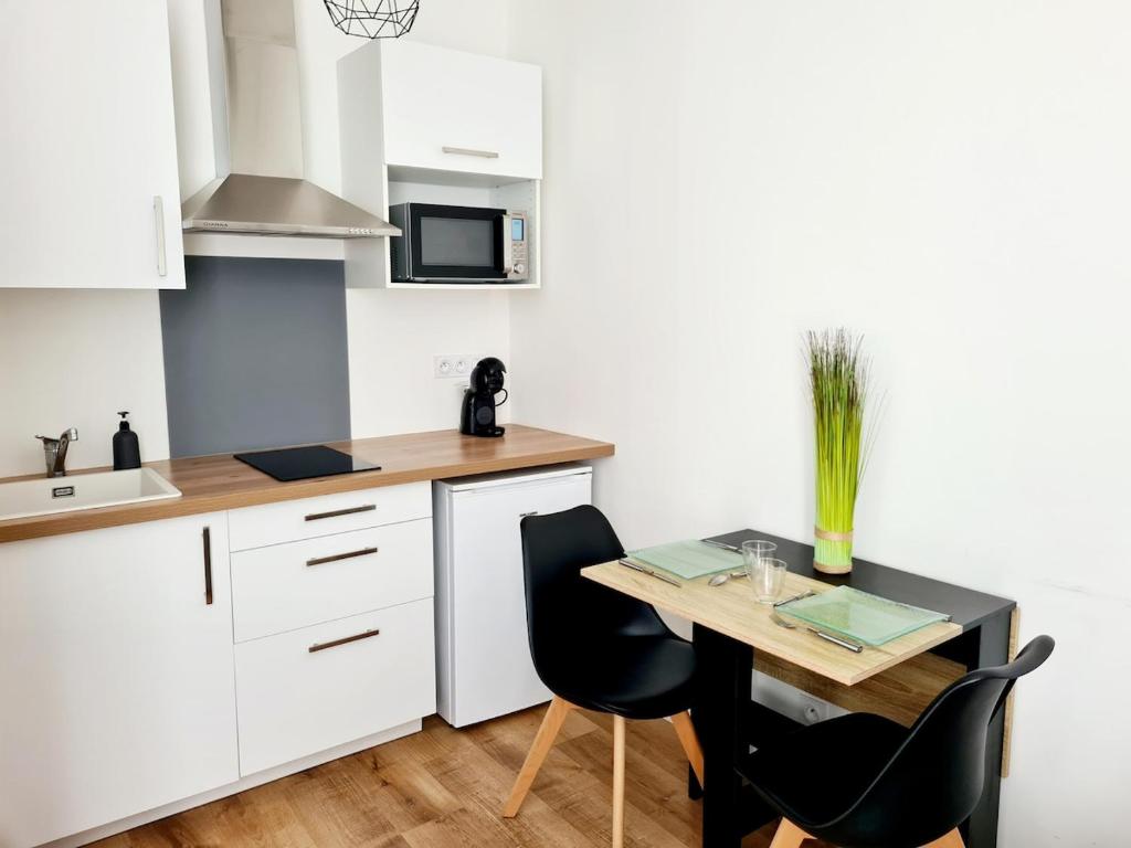 Una cocina con gabinetes blancos y una mesa con sillas. en Studio 2 Cosy en centre-ville - Puy duFou, en Les Herbiers